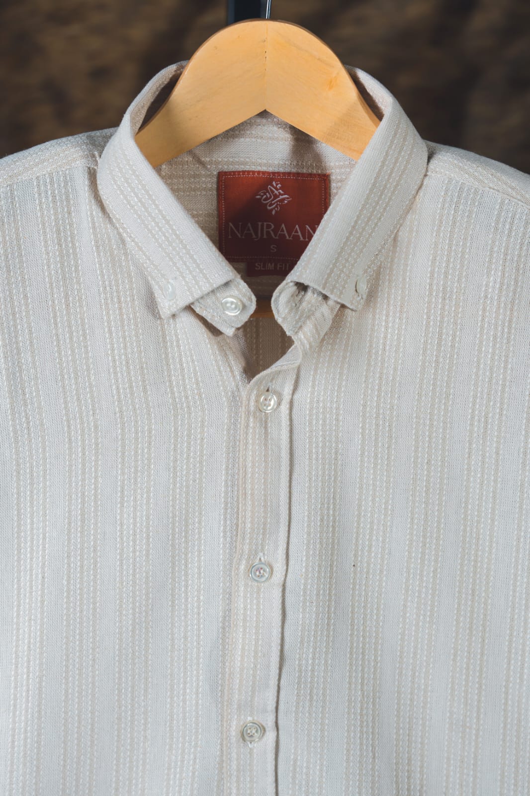 Light gray shirt with a visible brand label on a wooden hanger against a dark background