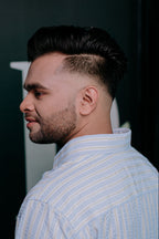 A man in profile wearing a light blue and white vertically striped button-down shirt, showcasing a modern fade haircut.