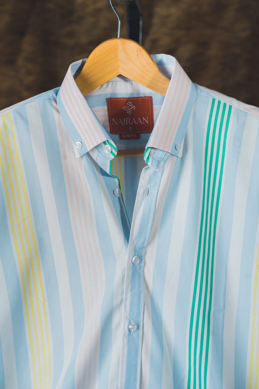Striped shirt with visible brand label on a wooden hanger against a blurred background