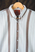 White shirt with brown accents on a hanger against a dark background