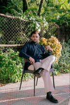 Front view of a man sitting outdoors in a navy blue tailored fit shirt and beige pants by Najraan