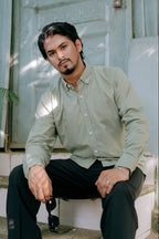 Man sitting outdoors in a sage green long sleeve solid shirt and black pants by Najraan